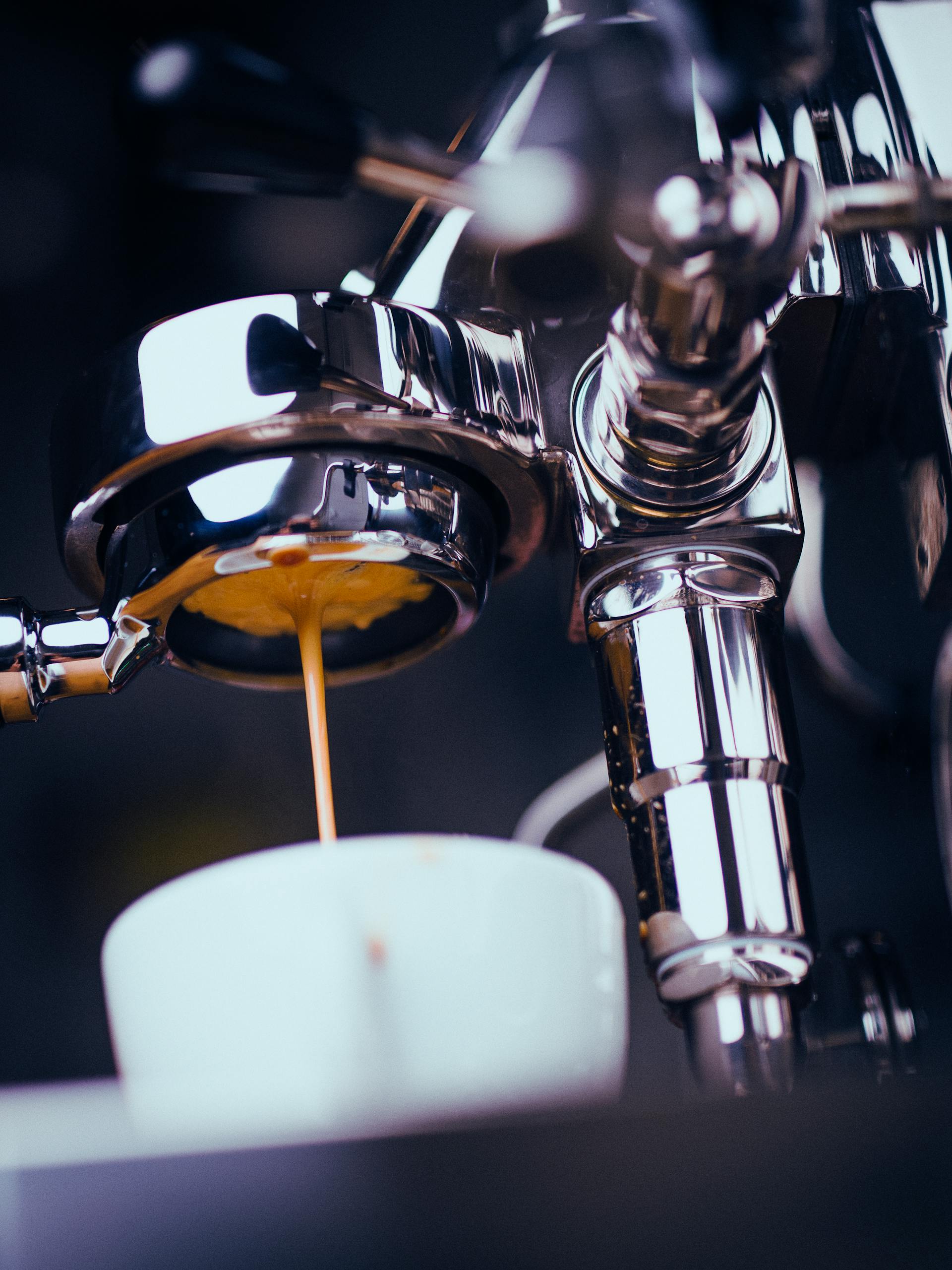 A shiny espresso machine brews coffee with an espresso shot pouring into a white cup.