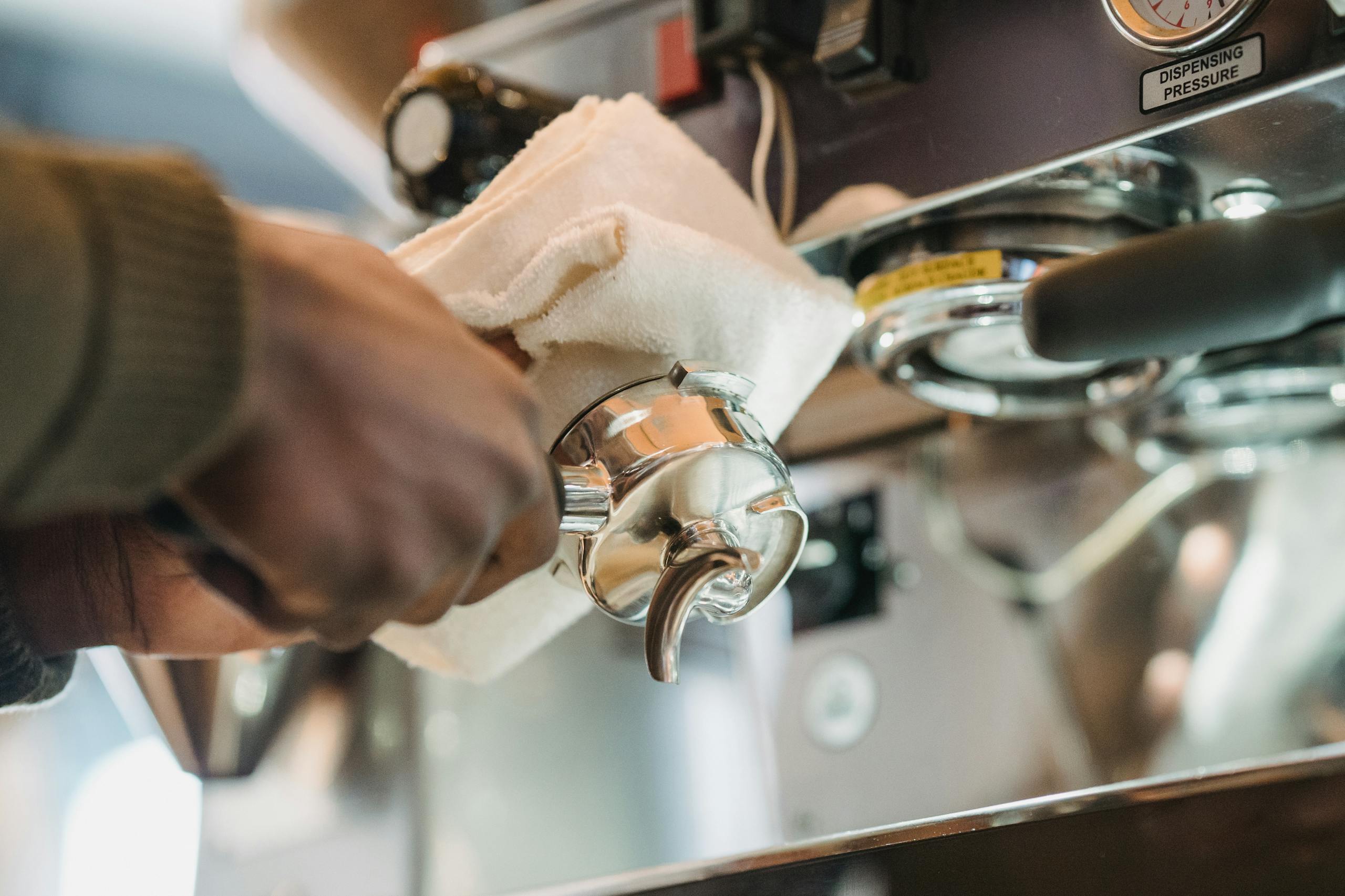 Close-up of barista cleaning a coffee machine portafilter with cloth for hygiene.