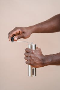 A close-up image of a person using a stainless steel grinder with a beige background.
