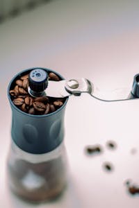 A close-up view of a manual coffee grinder filled with coffee beans.