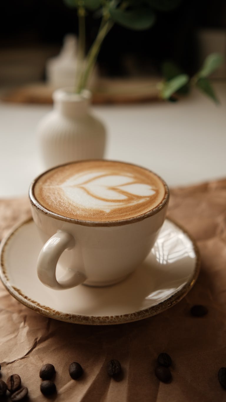 A close-up of a latte with froth art in a ceramic cup, surrounded by coffee beans.