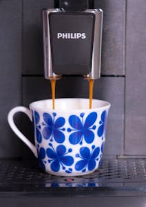 Close-up of coffee pouring into a floral ceramic cup from a Philips machine.
