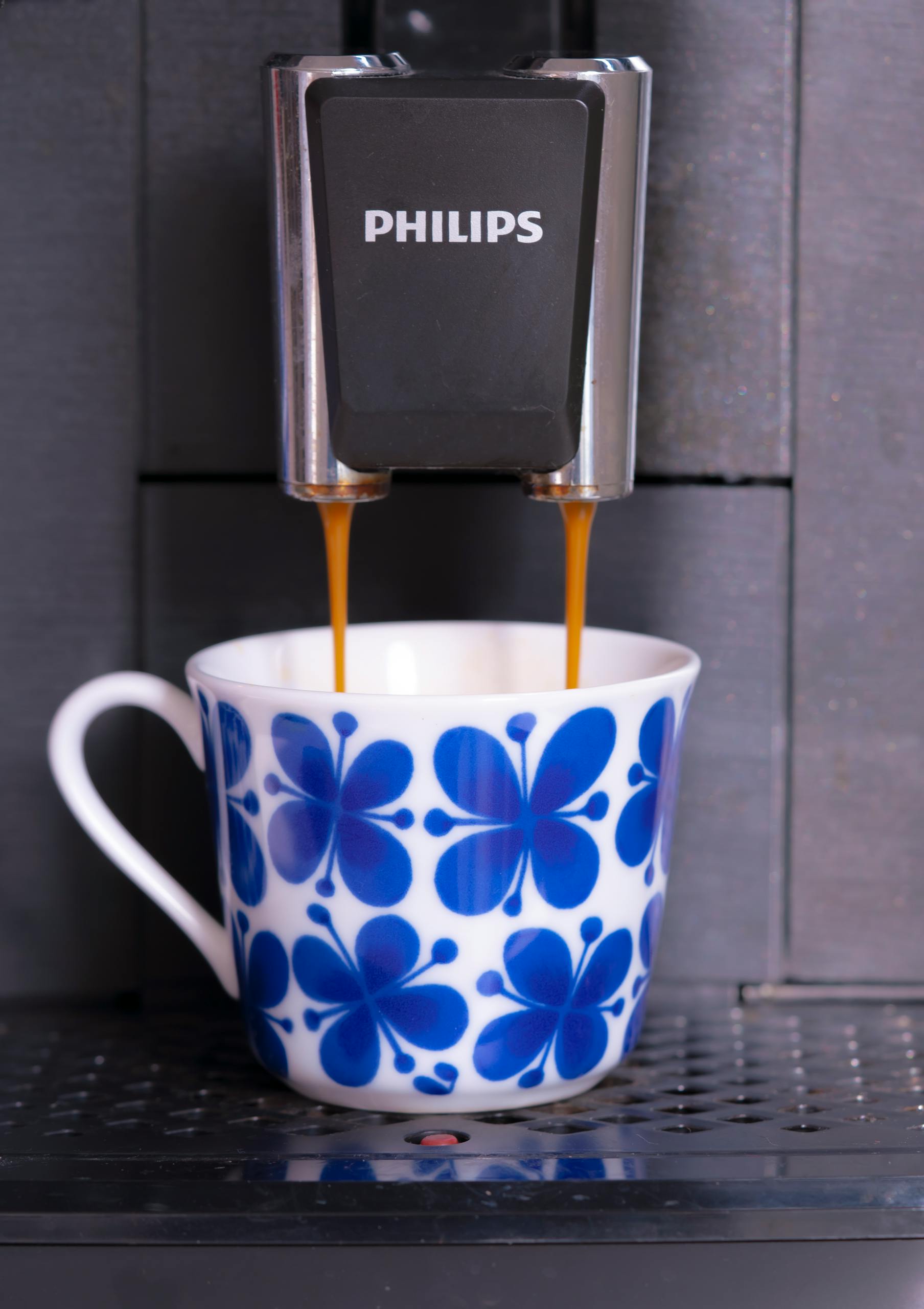 Close-up of coffee pouring into a floral ceramic cup from a Philips machine.