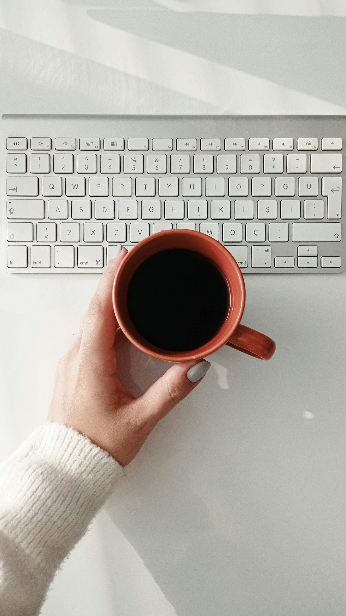Overhead view of a woman holding a coffee mug over a keyboard, symbolizing a work break.